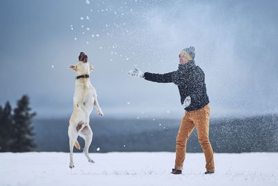 Man playing with dog on field during snowfall