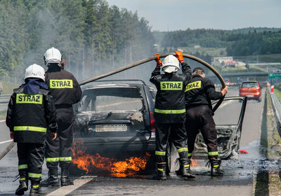Firefighters standing at burning car on road