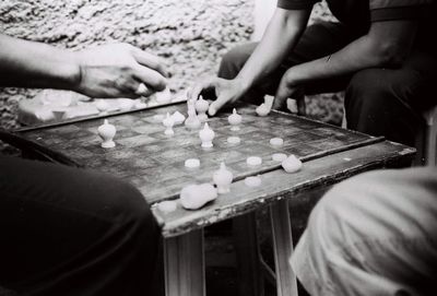 Midsection of friends playing board game while sitting outdoors