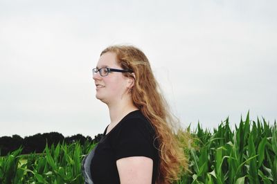 Side view of woman with long hair standing by crops at agricultural field