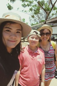 Portrait of smiling friends wearing hats standing on road against sky during sunny day