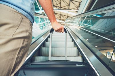 Cropped image of man holding luggage on escalator at airport