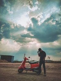 Rear view of man sitting on field against sky during sunset