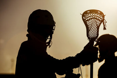 Silhouette man wearing sports clothing and helmet standing against sky during sunset