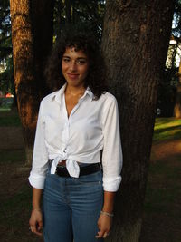 Portrait of smiling young woman standing by tree trunk