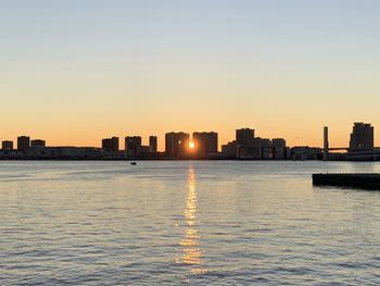 Sea and buildings against clear sky during sunset