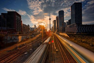 Railroad tracks amidst buildings in city against sky during sunset