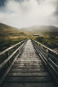 Boardwalk leading towards mountain against sky