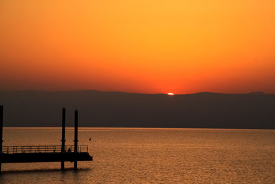 Silhouette wooden posts in sea against orange sky