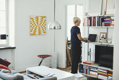 Rear view of product designer using laptop at shelf in home