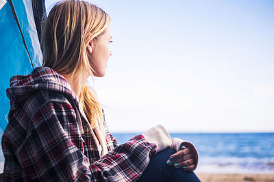 Young woman sitting at beach against clear sky
