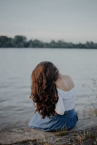 Woman sitting by lake against sky