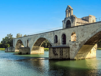 Arch bridge over river by building against sky