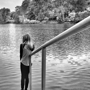 Rear view of girl standing by lake against railing