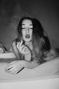 Woman smoking cigarette while lying on bed at home