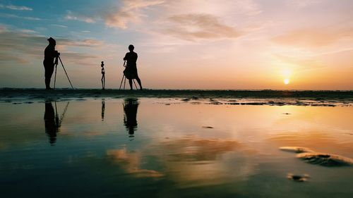 Silhouette people on beach against sky during sunset