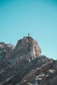 Low angle view of man standing on rock formation against clear sky
