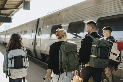 Rear view of family wearing backpacks while walking near train at railroad station