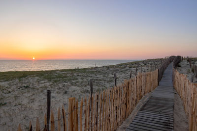 Walkway at beach against sky during sunset