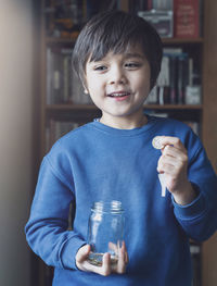 Smiling boy holding coin while standing at home