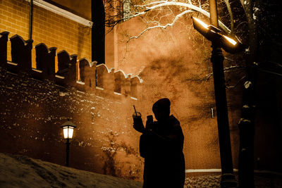 Rear view of silhouette man standing by illuminated building