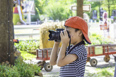 Boy photographing with camera while standing at park