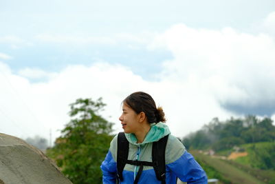 Side view of young woman standing against sky