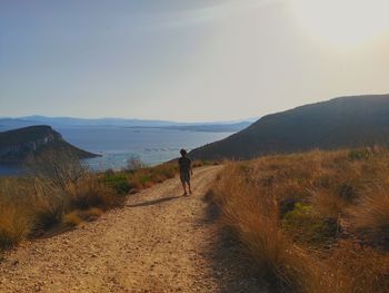 Rear view of man walking on mountain against sky