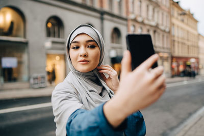 Confident young muslim woman taking selfie on city street