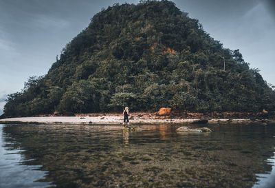 Rear view of woman standing at beach against mountain