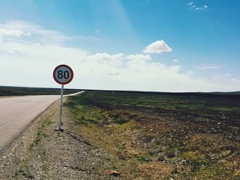 Road sign on field against sky