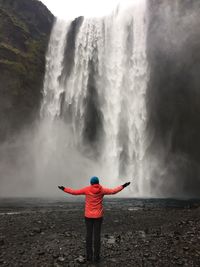 Rear view of woman standing against waterfall