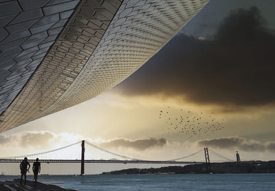 Suspension bridge over sea against cloudy sky