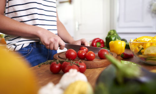 Midsection of teenage girl cutting tomatoes on kitchen counter