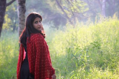 Young woman standing on field against trees