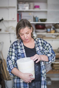 Mature female potter holding clay vase at workshop