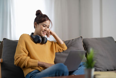 Young woman using mobile phone while sitting on sofa at home