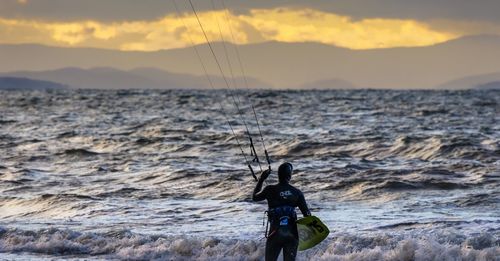 Rear view of person kiteboarding at sea shore against sky during sunset
