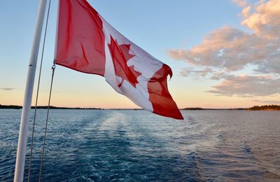 Close-up of canadian flag on lake against sky during sunset 