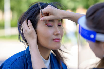 A pretty mongolian woman is being made up in a park by a make-up artist for a photo shoot.