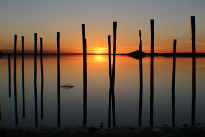 Silhouette wooden posts in sea against sky a sunset