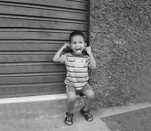 Boy sticking out tongue while sitting by closed shutter