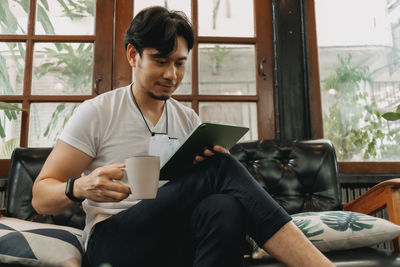 Young man using mobile phone while sitting on window