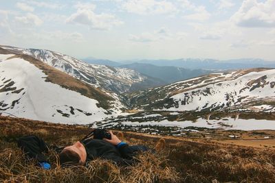 Man with camera relaxing on mountain against sky during winter