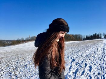 Side view of smiling woman standing on snow field against clear blue sky