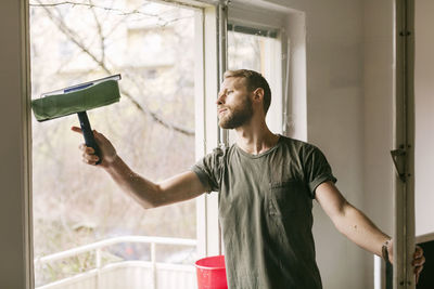 Young man looking through window at home