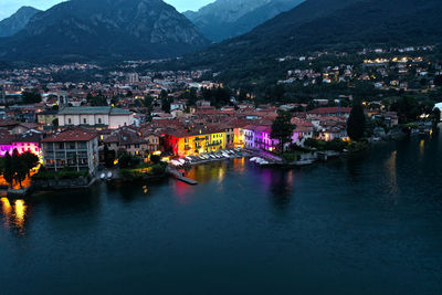 Illuminated city by river against sky at dusk