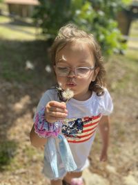 Young girl with windblown hair blowing dandelion into the wind.