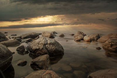 Rocks on shore against sky during sunset