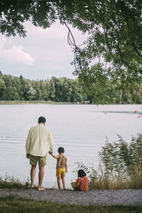Rear view of father holding hands with daughter standing against lake
